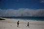 Røgen fra de mange brande, der har kostet mindst tre personer livet, kan ses på store strækninger af den australske østkyst. Her ses børn lege på stranden Forster i New South Wales, mens røgen fra brandene tårner sig op i horisonten.
