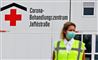 En hospitalsmedarbejder med maske på foran et corona-skilt