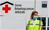 En hospitalsmedarbejder med maske på foran et corona-skilt