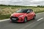 En rød Toyota Yaris med grønne marker i baggrunden.