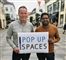 To mænd står på en gågade med et skilt, hvor der står Pop Up Spaces på