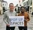 To mænd står på en gågade med et skilt, hvor der står Pop Up Spaces på