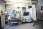 En hospitalsstue, hvor to læger eller sygesplejersker står ved en hospitalsseng med engangskitler, hårnet, handsker og masker på. 