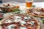 To lune pizzaer med smeltet os på et bord og en øl bagved