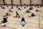 I en gymnastiksal ligger en masse mennesker på tynde madrasser og laver gymnastik