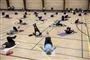 I en gymnastiksal ligger en masse mennesker på tynde madrasser og laver gymnastik