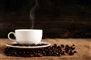 rygende kaffekop på underkop omgivet af kaffebønner