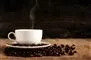 rygende kaffekop på underkop omgivet af kaffebønner