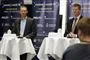 Billede af Erik Brøgger ved onsdagens pressemøde. Han står ved et højt cafébord med en hviddug. Ved et andet bord ved siden af ses Søren Brostrøm