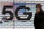 En mand taler i telefon foran et stort 5G-skilt
