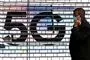 En mand taler i telefon foran et stort 5G-skilt
