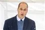 Nærbillede af prins William. Han har høje tændinger og er klædt i hvid skjorte med et sort slips, en lyseblå trøje og en mørkeblå blazer.