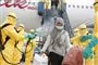 Flypassagerer bliver sprøjtet af folk i gule sikkerhedsdragter da de forlader et fly. 