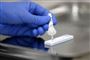 En hånd i en blå latexhandske trykker væske fra en pipette ud i en test.