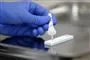 En hånd i en blå latexhandske trykker væske fra en pipette ud i en test.