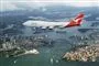 En jumbojet flyver hen over Sydney havn med operahuset og broen nedenunder.