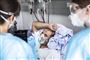 person med mundbind ligger i hospitalsseng