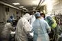 en masse læger og sygeplejersker iført værnemidler står om en hospitalsseng. 