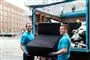 To smilende yngre mennesker slæber en sofa ind i en lastbil
