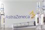 glas og injektionssprøjte ligger på bord foran logo fra astrazeneca
