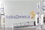 glas og injektionssprøjte ligger på bord foran logo fra astrazeneca
