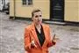 Mette Frederiksen i orange habit med gestikulerende arme og alvorlig mine. 