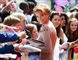 Sarah Harding giver autografer til en stor skarer af folk mens hun smiler direkte ind i kameraet. 