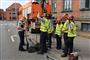 En masse mænd i neonfarvede veste og en politibetjent ved et kloakhul.