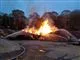 Flere brandmænd arbejder på at slukke flammerne fra hver sin side af et stort brandende bål