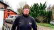 En mand med fleece trøje og tophue foran en gård med blandt andet et grantræ
