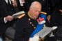 Kong Harald med en stor hvid folder som han kigger i.