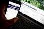 person sidder med telefon foran computer