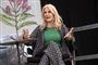 Helle Thorning-Schmidt i blomstret jakkesæt og en grøn bluse. Hun sidder på en scene og taler
