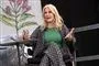 Helle Thorning-Schmidt i blomstret jakkesæt og en grøn bluse. Hun sidder på en scene og taler