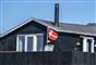 et gammelt sommerhus med et slidt Dannebrog foran