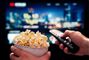 Mand ser Tv med en skål popcorn i hånden