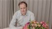 portræt af knud romer siddende bag en buket blomster og foran en grå bagvæg