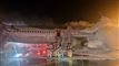 Brandmænd der står på jorden og sprøjter vand på et fly fyldt med røg
