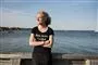 Kvinde med vind i håret og armene over kors med havet som baggrund
