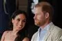 Meghan i sommerkjole læner sig smilende mod Harry i lys jakke og skjorte