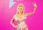 Dolly Parton iført pink spøjs kjole, med stort smil og hånden hævet til  hilsen. 