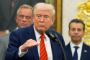 Trump taler foran en mikrofon med nogle folk bag sig. 