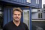 Bjarke Ingels står foran blåt træskur og kigger i kameraet
