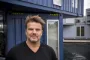 Bjarke Ingels står foran blåt træskur og kigger i kameraet