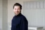 Simon Stenspil i mørk sweater mod en hvid baggrund