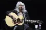 Emmylou Harris med en guitar på knæet siddende foran en mikrofon