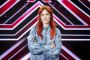 Oh Land i blå denimskjorte smilende med armene over kors stående foran X Factor-scenografi
