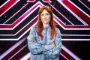 Oh Land i blå denimskjorte smilende med armene over kors stående foran X Factor-scenografi