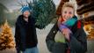 Lene og Anders Beier står i sne uden for en træhytte med et juletræ med lys på i baggrunden