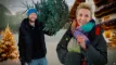 Lene og Anders Beier står i sne uden for en træhytte med et juletræ med lys på i baggrunden